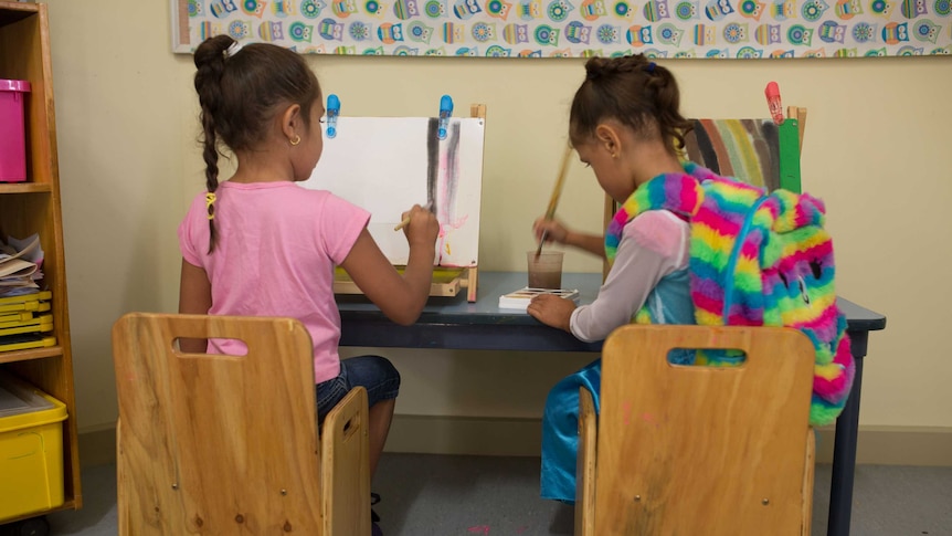 Two girls sitting down and painting during class.