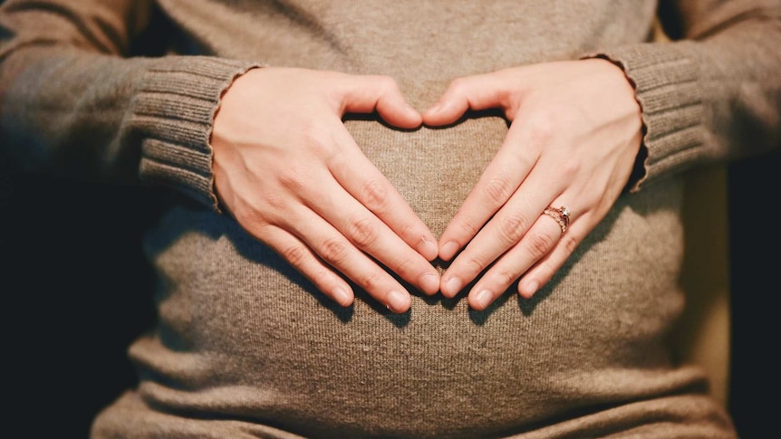 Pregnant woman with hands in heart shape on belly
