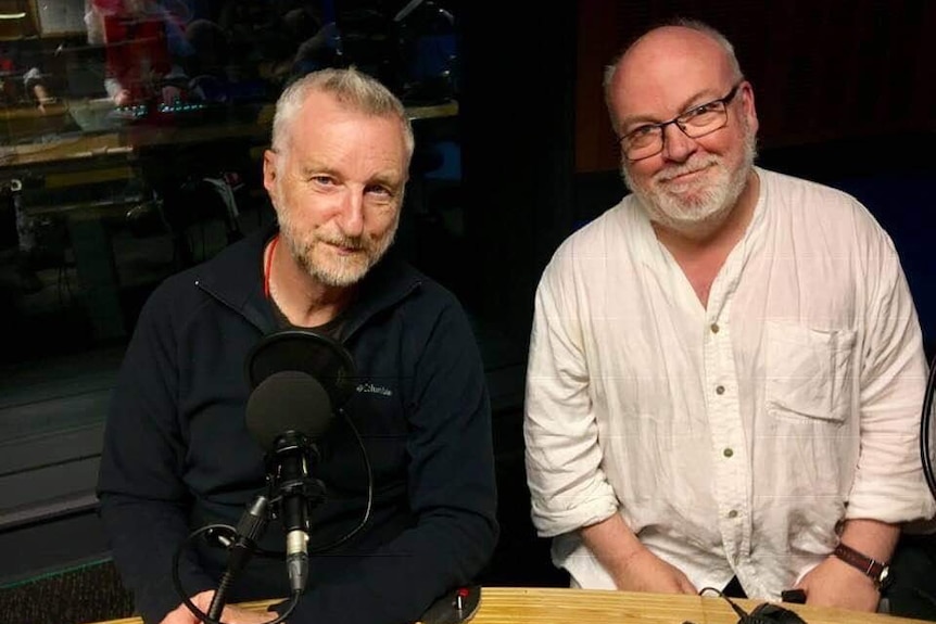 Two men looking to camera sitting in radio studio.