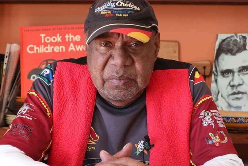 Archie Roach sits in front of bookshelf