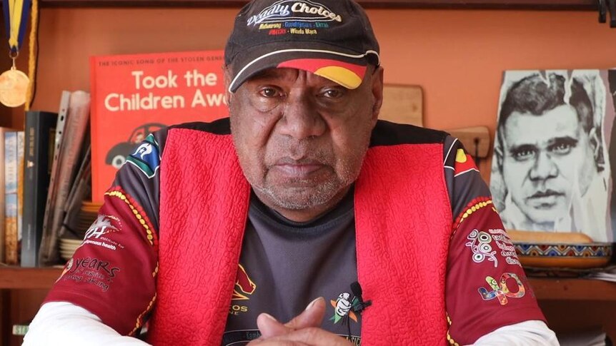 Archie Roach sits in front of bookshelf