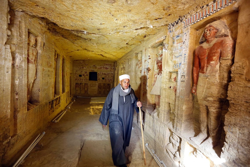 Mustafa Abdo, chief of excavation workers, walks in recently uncovered tomb with statues and hieroglyphics on the walls.