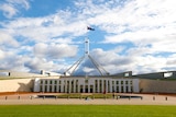 The front entrance of Parliament House, in the daytime, with flag raised and people walking around.