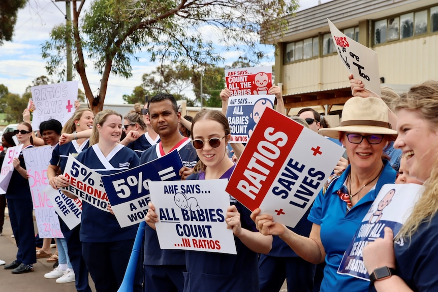 Nurses gather outside a hospital waving signs