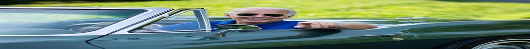 乔·拜登，穿着蓝色马球衫和飞行员墨镜从方向盘后面指向相机f 绿色敞篷车