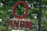 A cut out cardboard sign reading "QANON".