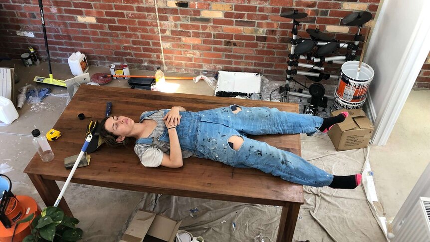 A woman lying on a table surrounded by mess from renovating