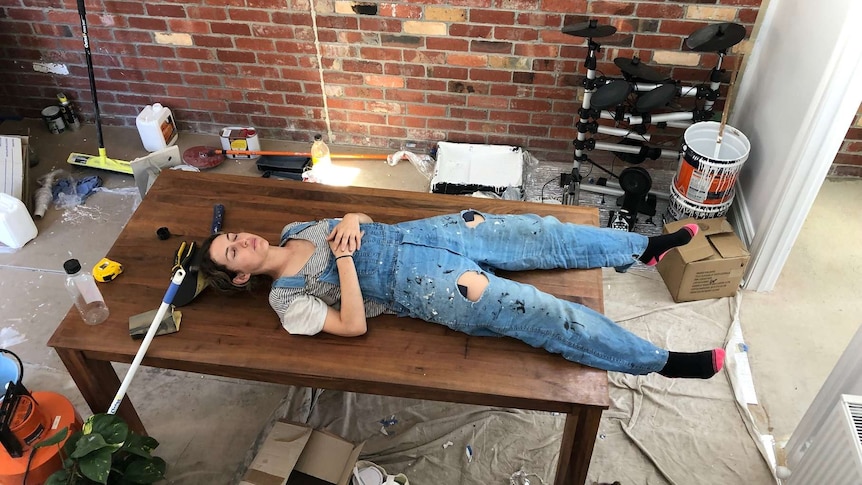 A woman lying on a table surrounded by mess from renovating