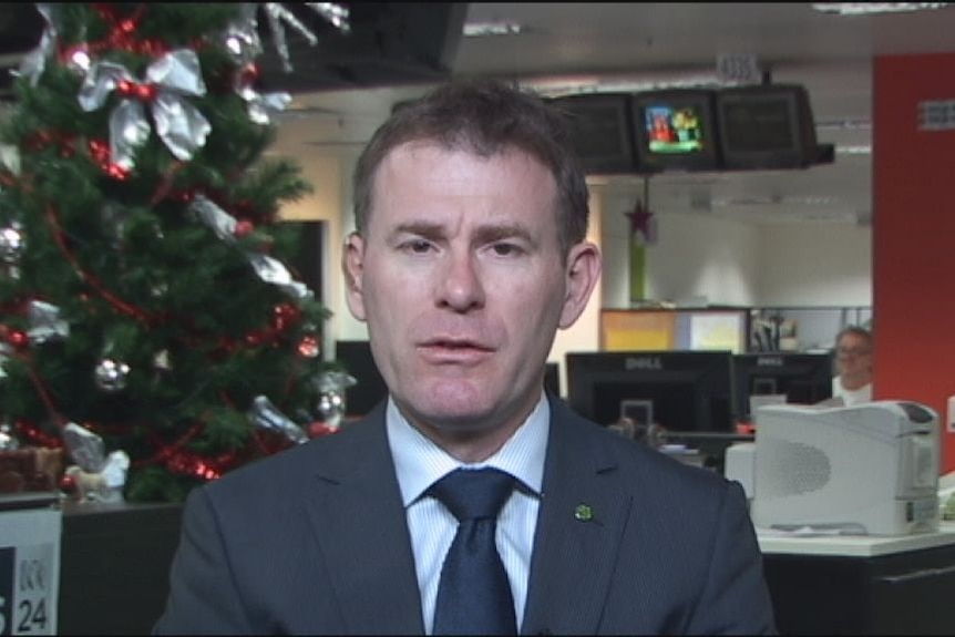 A man wearing a suit sitting in front of a Christmas tree