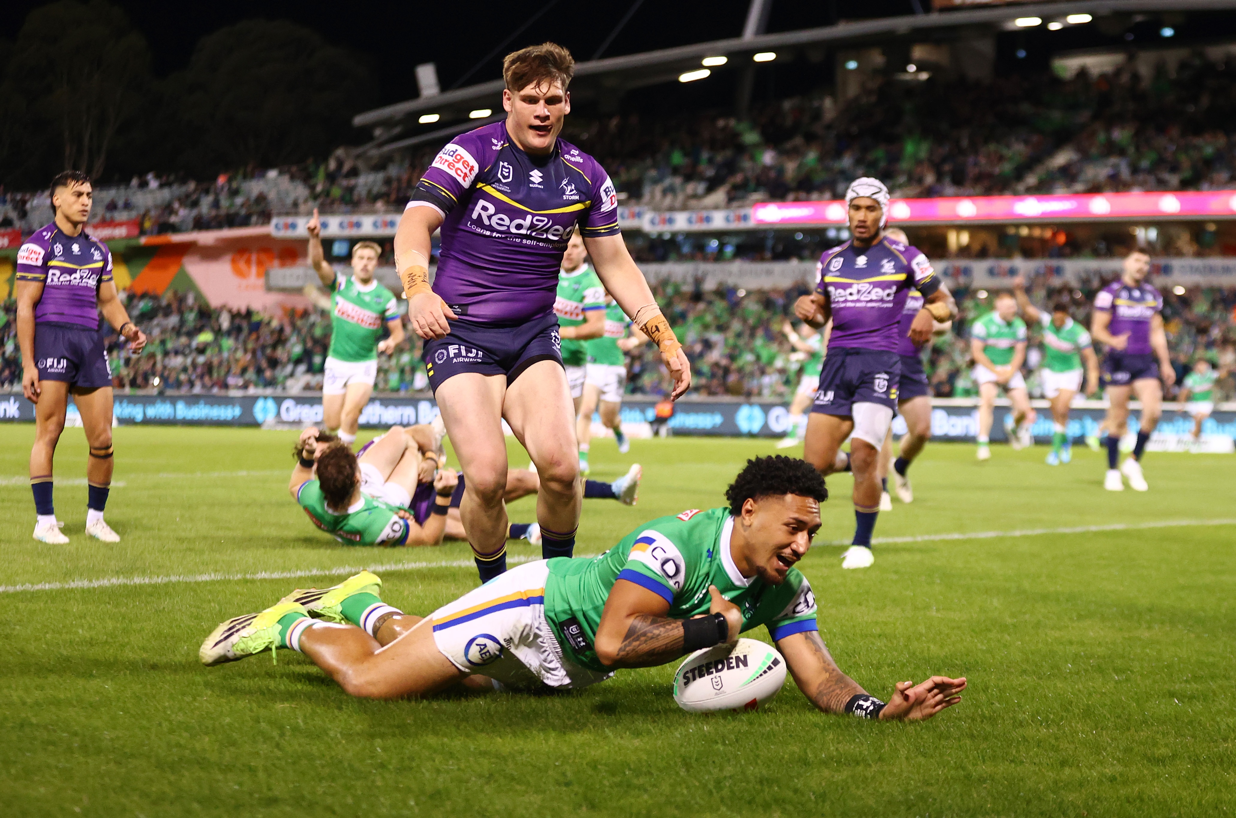 A rugby league player in green scores a try with players in purple behind him