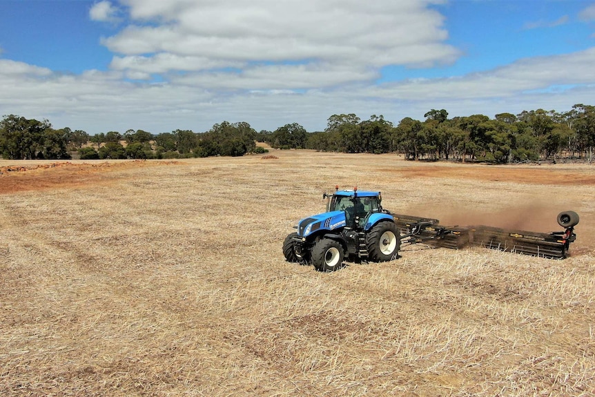 Tractor harvests dry grass in a brown paddock.