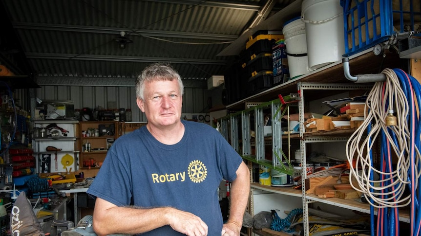A mid-shot of a man in a rotary shirt leaning on a drop saw