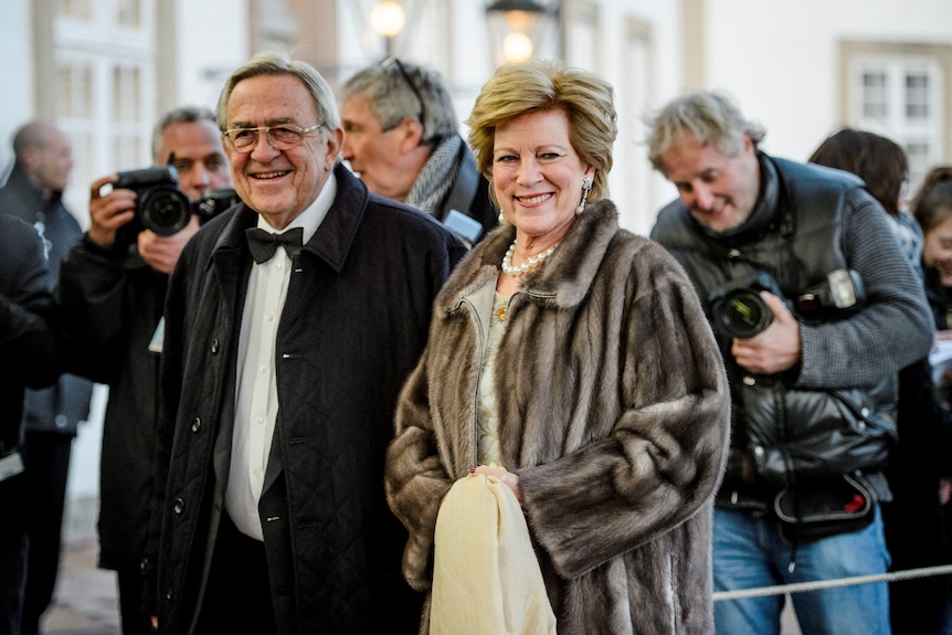 King Constantine dressed in a suit standing next to Queen Anne-Marie. 