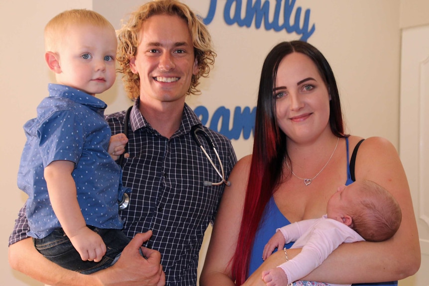 Male midwife Christian Wright and mother Sonya McGuire pose for a photo holding two-year-old Archer and three-week-old Imogen.