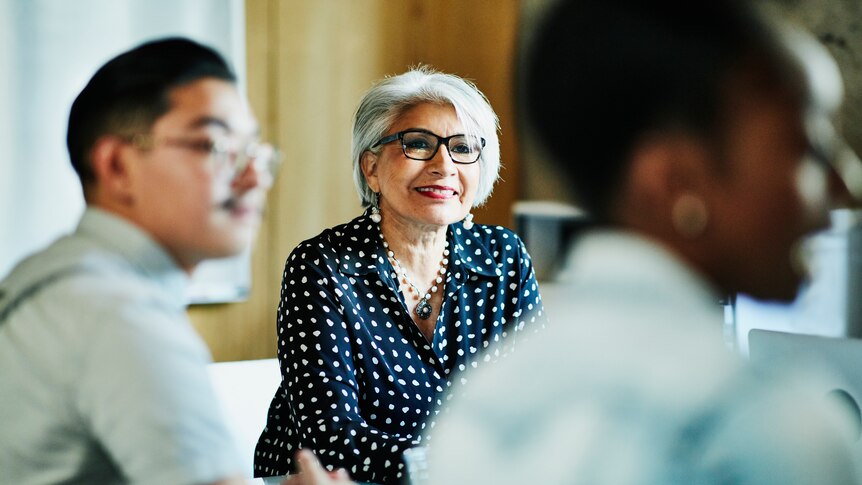 Smiling mature female businesswoman surrounded by co-workers.