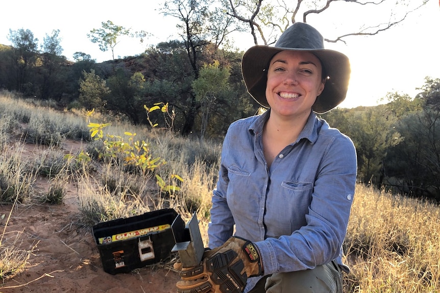 A woman holding a metal device in her hands, crouching in the outback.