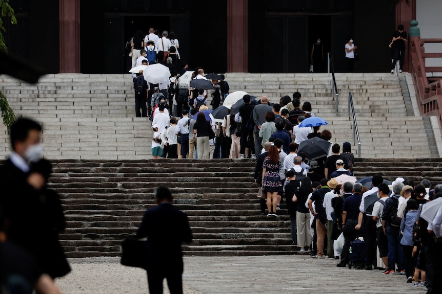 A long line of people at steps of temple