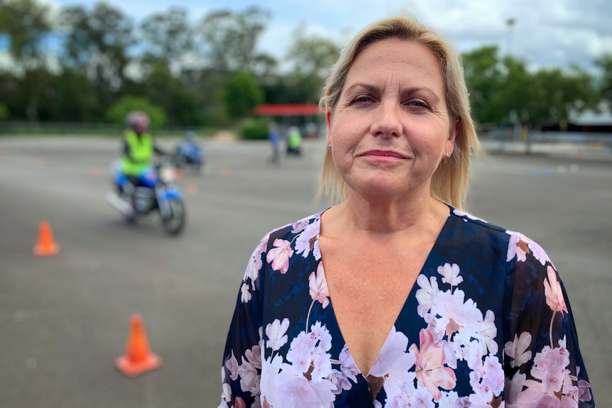 Marnie Dennis stands outside with a learner motorcyclist riding behind her in a training exercise.