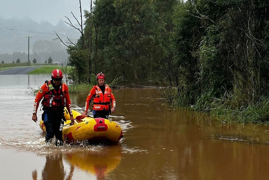 SES crews in Lismore with rubber boat on flooded roadway, grey skies and rain and trees in the background