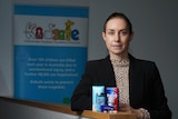 A woman in a blazer stands behind nicotine and vaping products in front of the KidSafe sign
