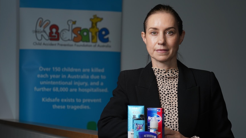 A woman in a blazer stands behind nicotine and vaping products in front of the KidSafe sign