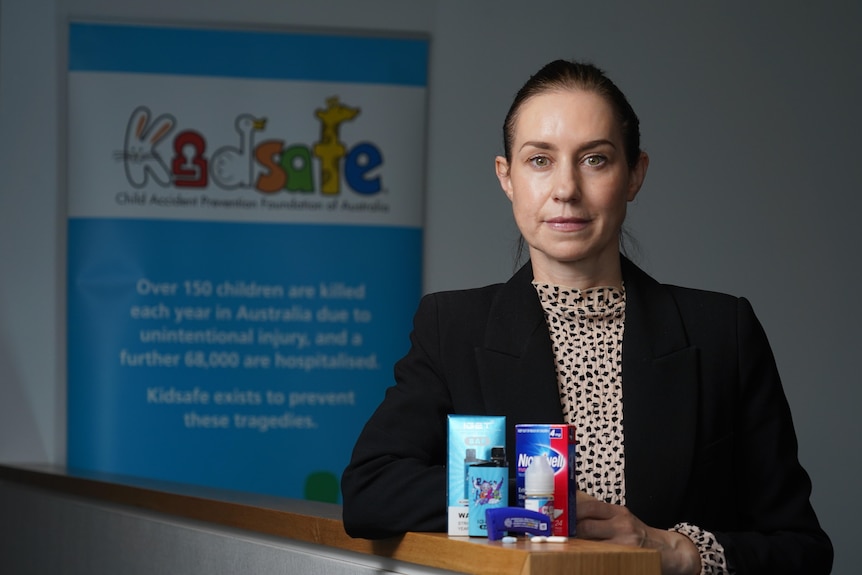 A woman in a blazer stands behind nicotine and vaping products in front of the KidSafe sign