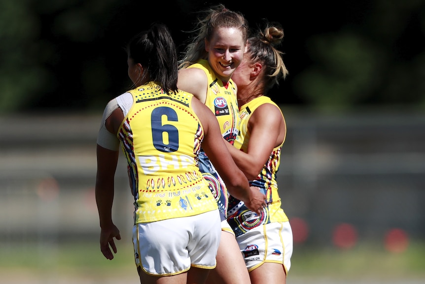 Three Adelaide Crows AFLW players celebrate a goal.