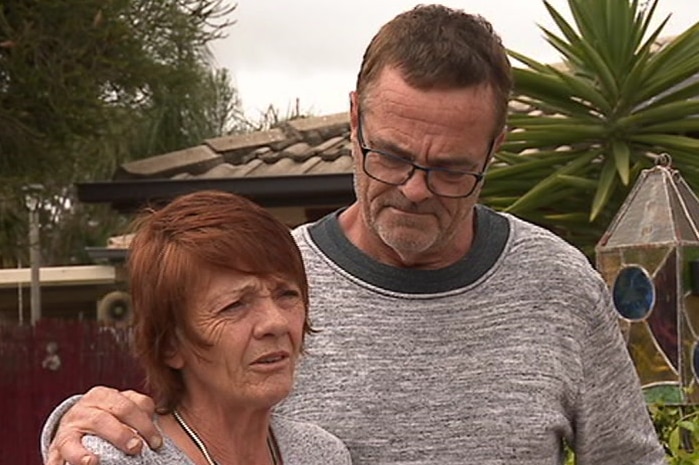 A woman and a man with microphone stands in front of a house