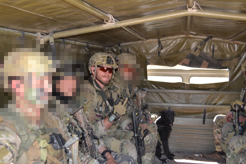 A soldier is pictured in a vehicle surrounded by fellow soldiers whose faces are pixelated.