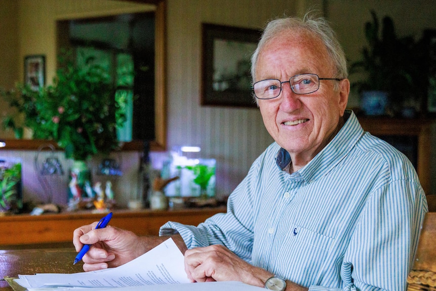 Keith Loveridge sits at a kitchen table, writing in a book.