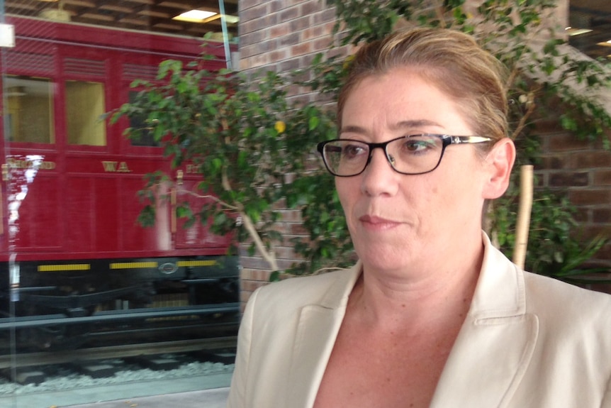 A woman wearing glasses standing near a display of a historic train.