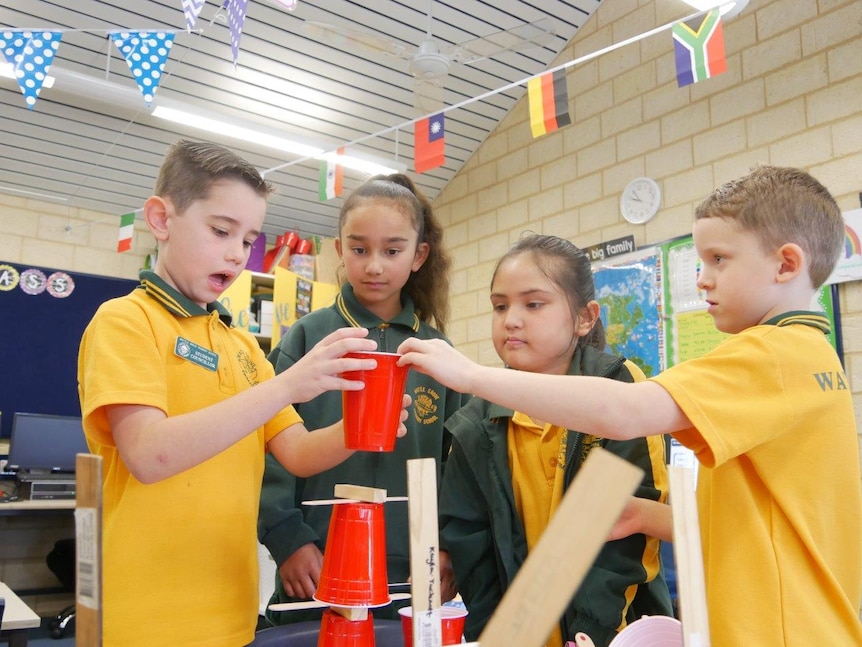 Four primary school students in a classroom using plastic cups on a table.