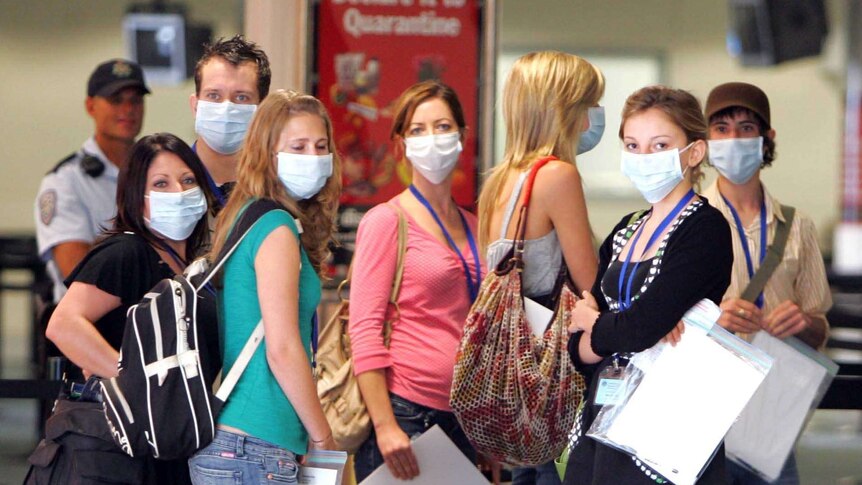 A group of passengers with face masks look at the camera.