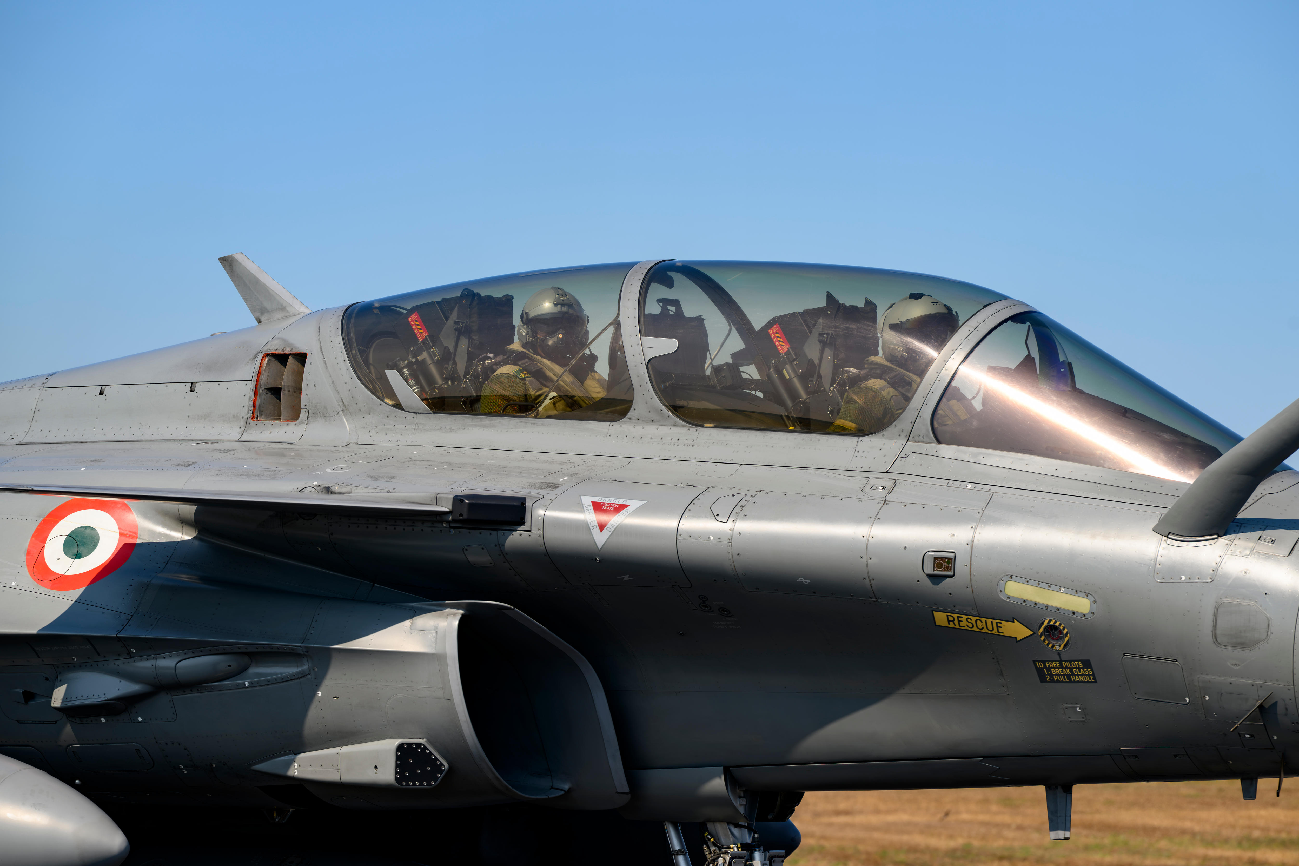 Pilots sit in the cockpit of a fighter jet.
