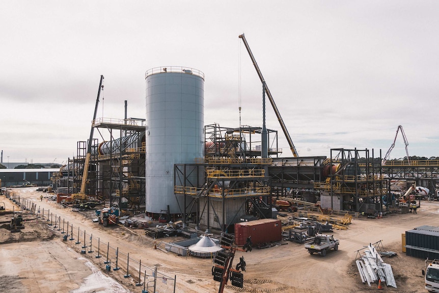 A large silo-like structure, with cranes around it and pipes.