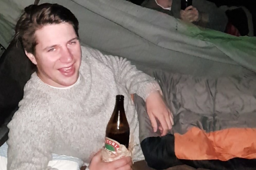 A man in a tent holding a beer bottle