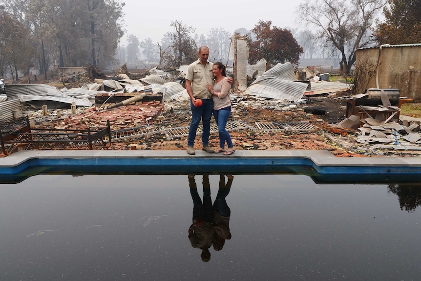 Matt and Katie Zagami standing by the swimming pool of their burnt out house. corrugated iron and bricks and burnt fences.