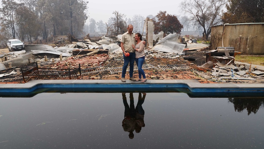 Matt and Katie Zagami standing by the swimming pool of their burnt out house. corrugated iron and bricks and burnt fences.