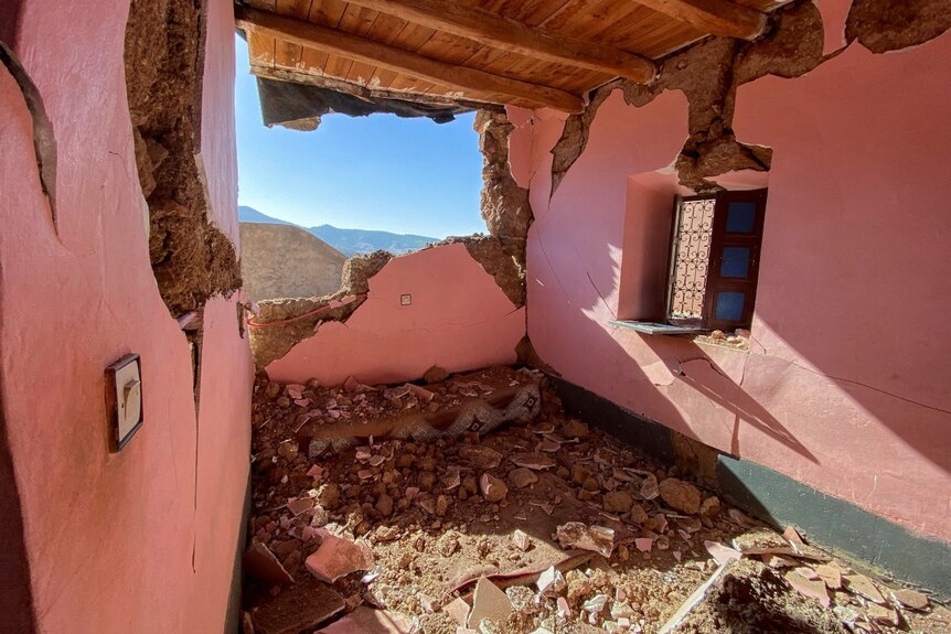 A mountain range can be seen in the distance out of the window of a damaged building.
