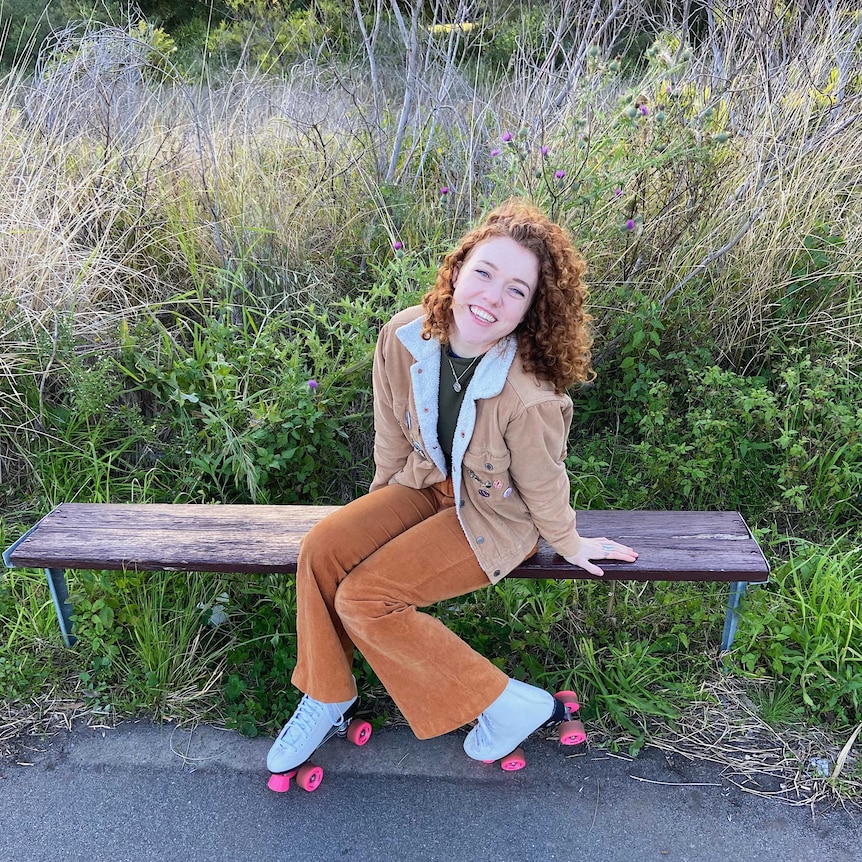 Emily sitting on a park bench wearing roller-skates.