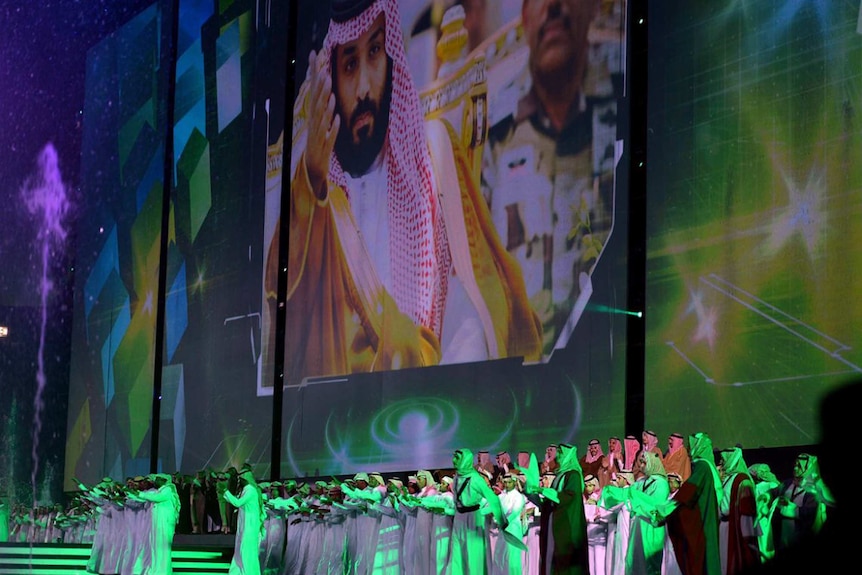 Saudi men perform under a giant screen showing an image of Saudi Crown Prince Mohammed Bin Salman
