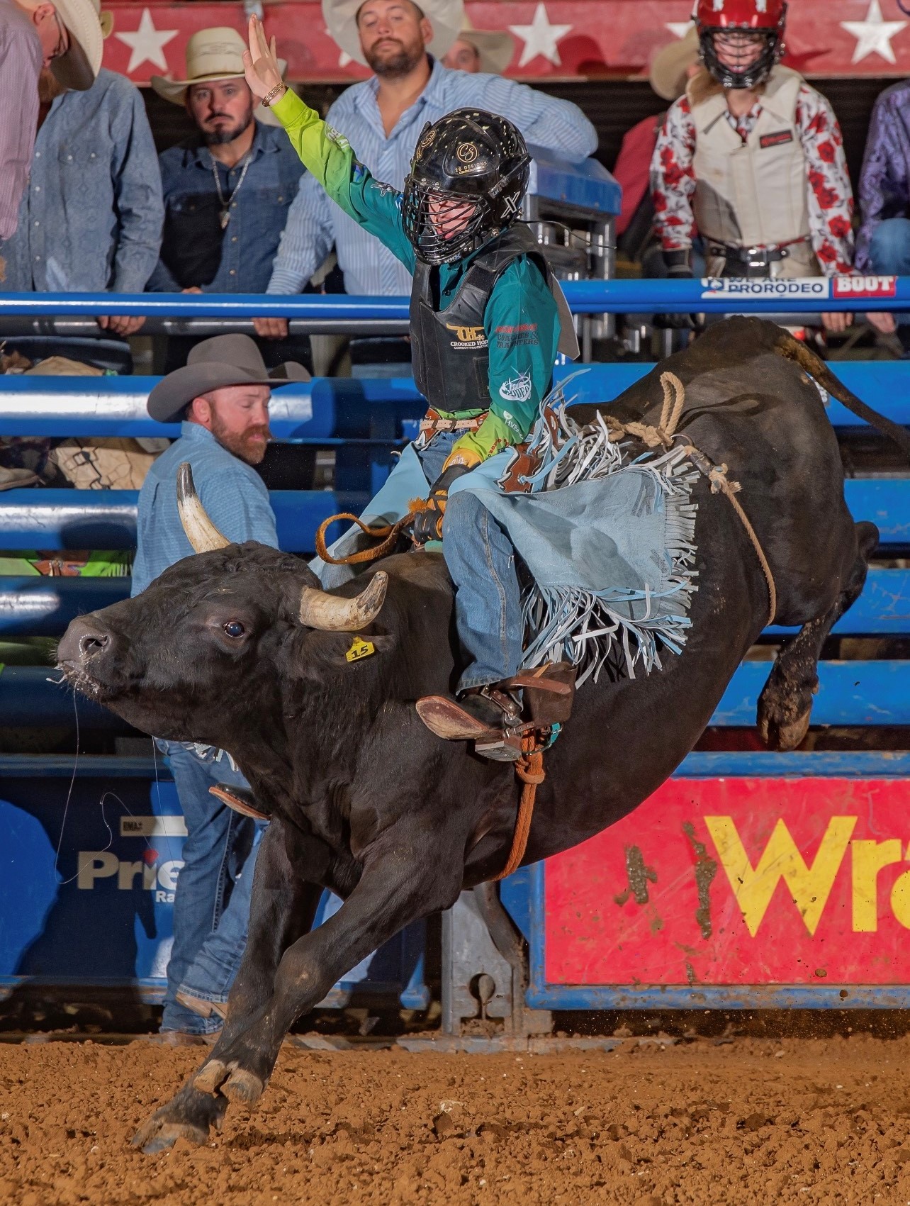 young boy riding a bucking bull wearing helmet and cowboy gear at a rodeo in Texas