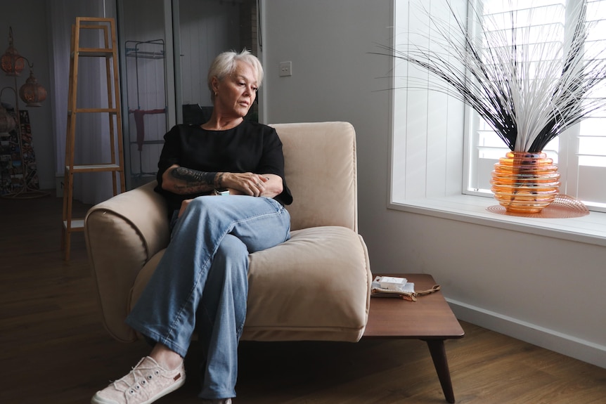 A woman sitting on a chair looking down to her side, with a sad expression on her face.