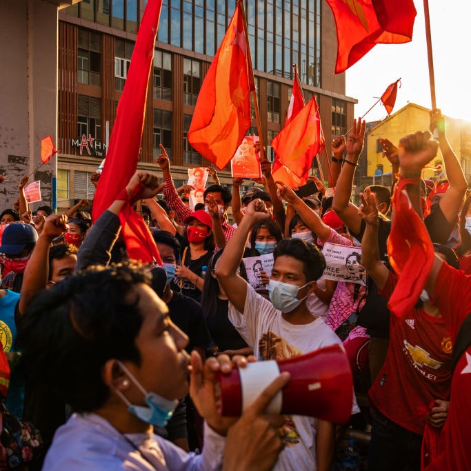 Protesters shout slogans while carrying red flags on February 07, 2021 in downtown Yangon, Myanmar