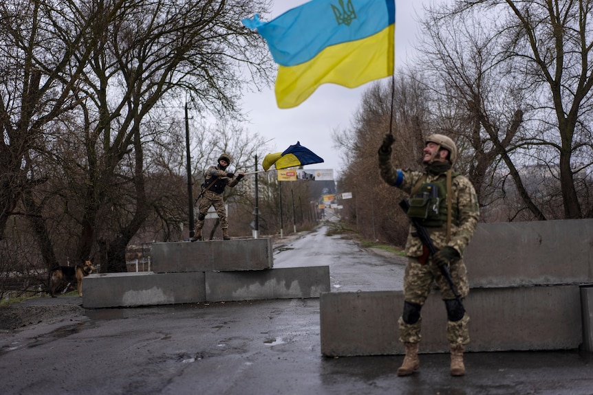 Two soldiers wave yellow and blue flags, smiling.
