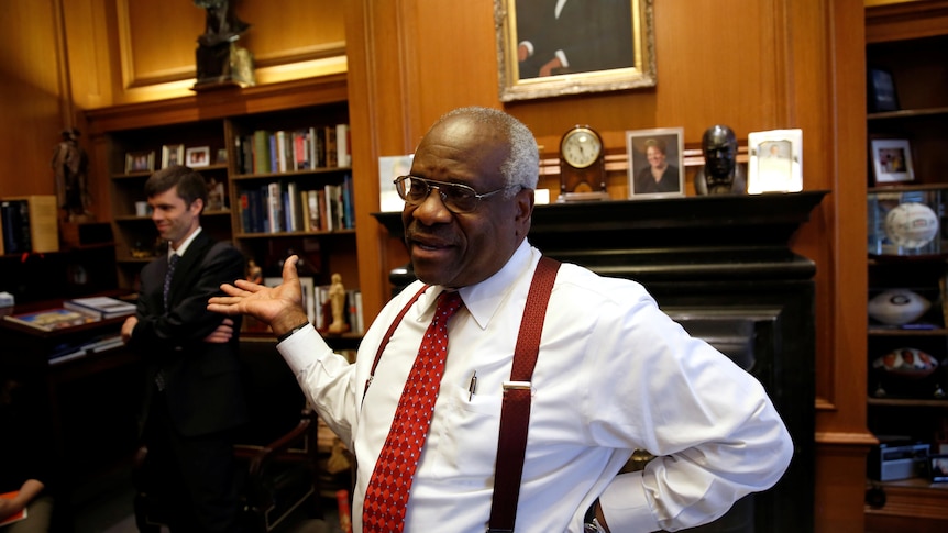 Clarence Thomas in shirtsleeves and suspenders gesturing in his office while talking