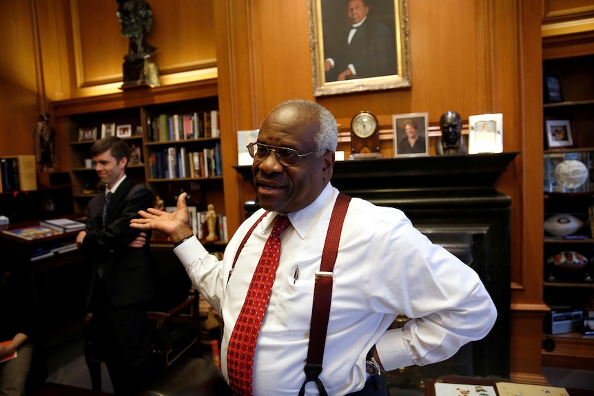 Clarence Thomas in shirtsleeves and suspenders gesturing in his office while talking