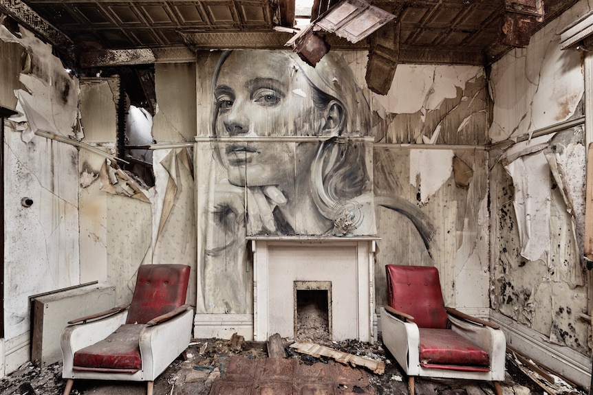 A female face looks down from a wall covered in peeling paint
