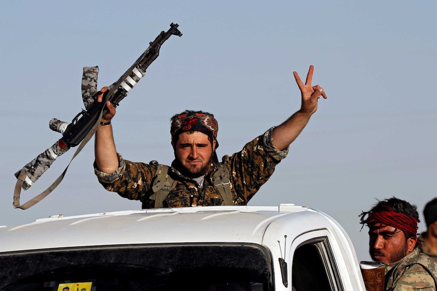 A fighter on the back of a truck makes a V-sign and holds his rifle in the air.