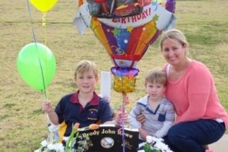 A woman with two children at the site of a baby's grave, with balloons and flowers.